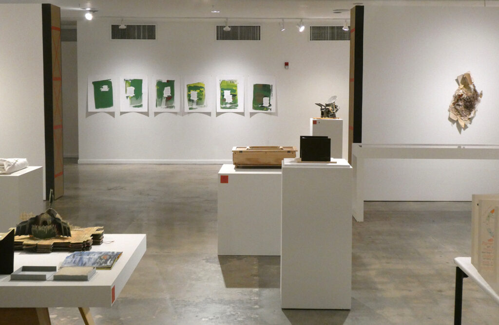 This image depicts a distanced view of BookBound from the center of the gallery looking towards the entrance; works on on the walls and also on pedestals.